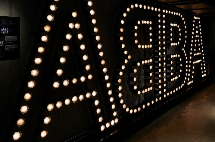 Large illuminated ABBA sign lights up a dark museum hallway.