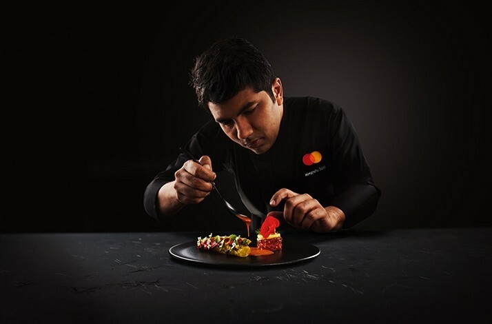 The chef wearing the uniform with the branded MC logo in the process of preparing the dish. has context menu