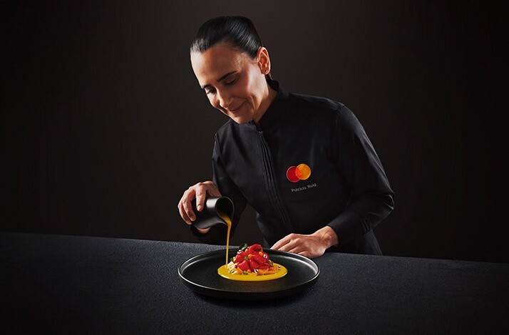 The chef wearing the uniform with the branded MC logo in the process of preparing the dish.