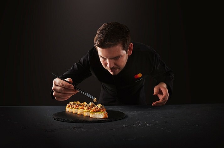 The chef wearing the uniform with the branded MC logo in the process of preparing the dish. has context menu