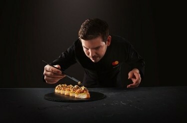 The chef wearing the uniform with the branded MC logo in the process of preparing the dish. has context menu
