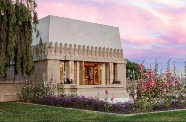 Outdoor exterior of Frank Lloyd Wright's Hollyhock House, surrounded with greenery and flowers.