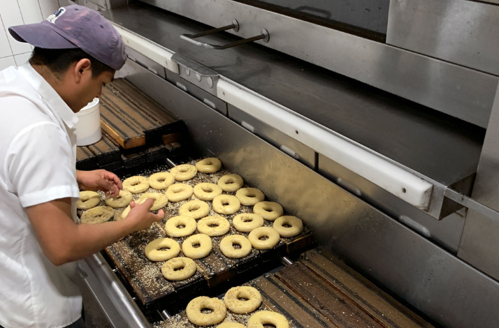 A baker is seasoning the bagels at Russ & Daughters. 