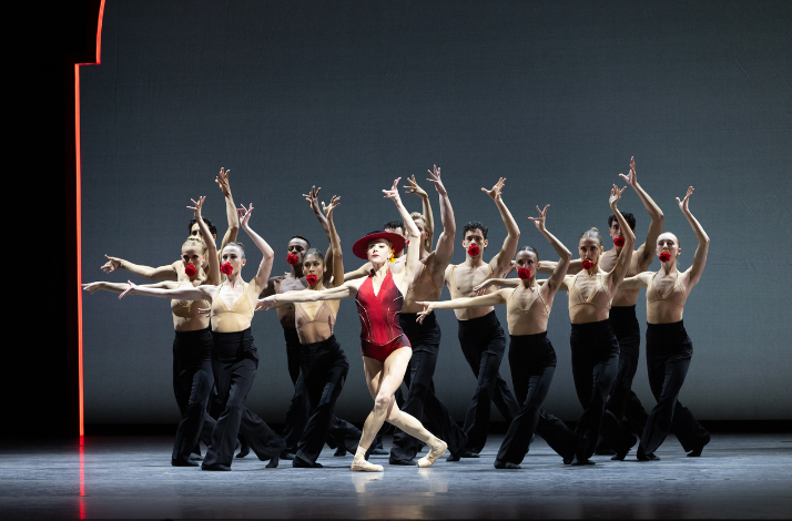 Ballet dancers in dramatic pose, center in red costume, arms raised on stage.